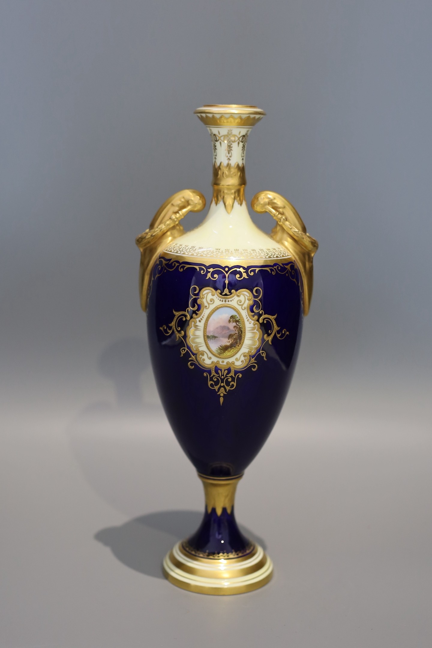 An early 20th century Coalport porcelain vase painted with a view of lake Windermere on a cobalt blue and ivory ground, height 29 cms.